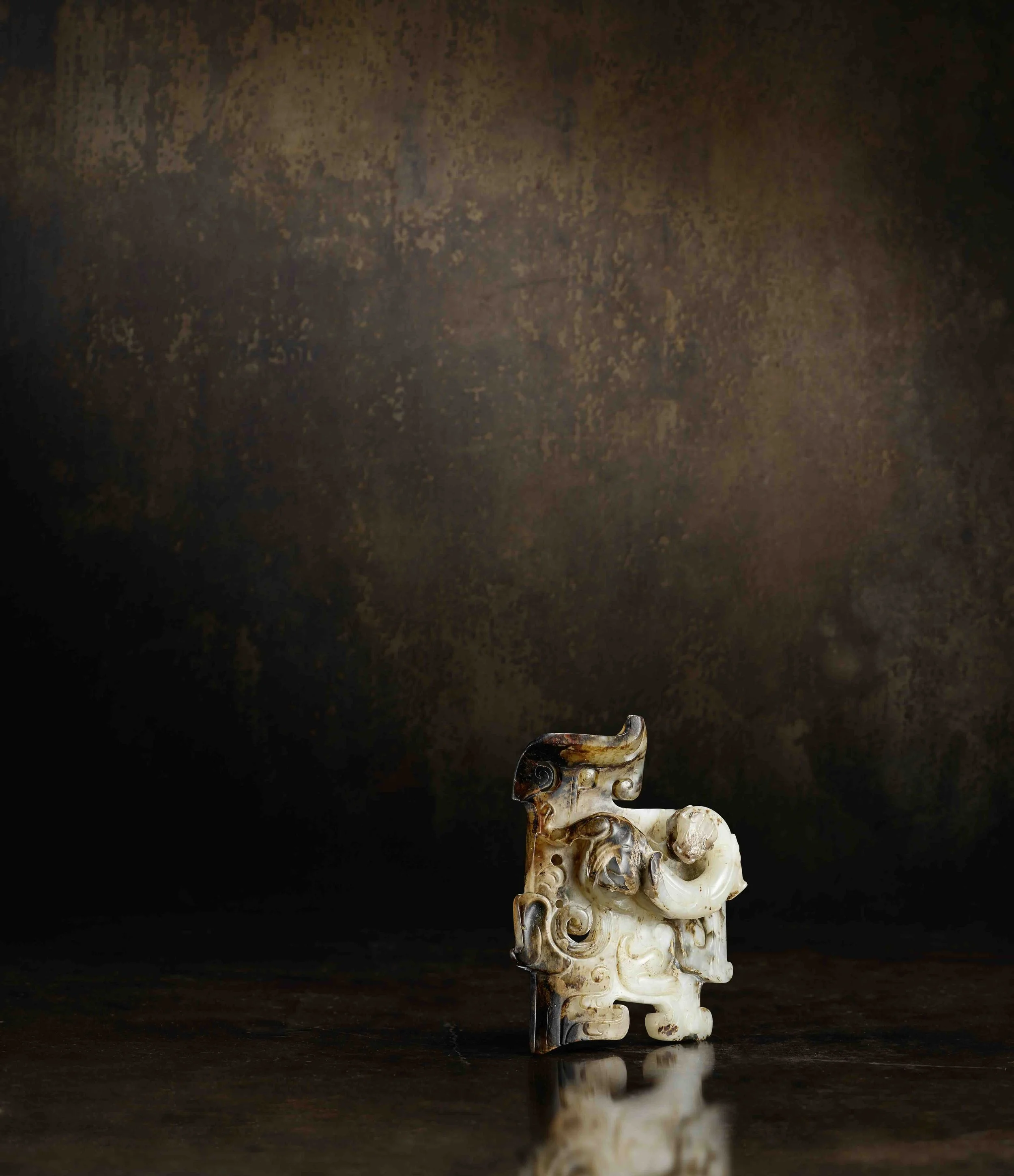 A mottled cream, pale grey and russet jade plaque carved in high relief with a coiled dragon, 
China: Western Han dynasty (206 BCE-9 CE)