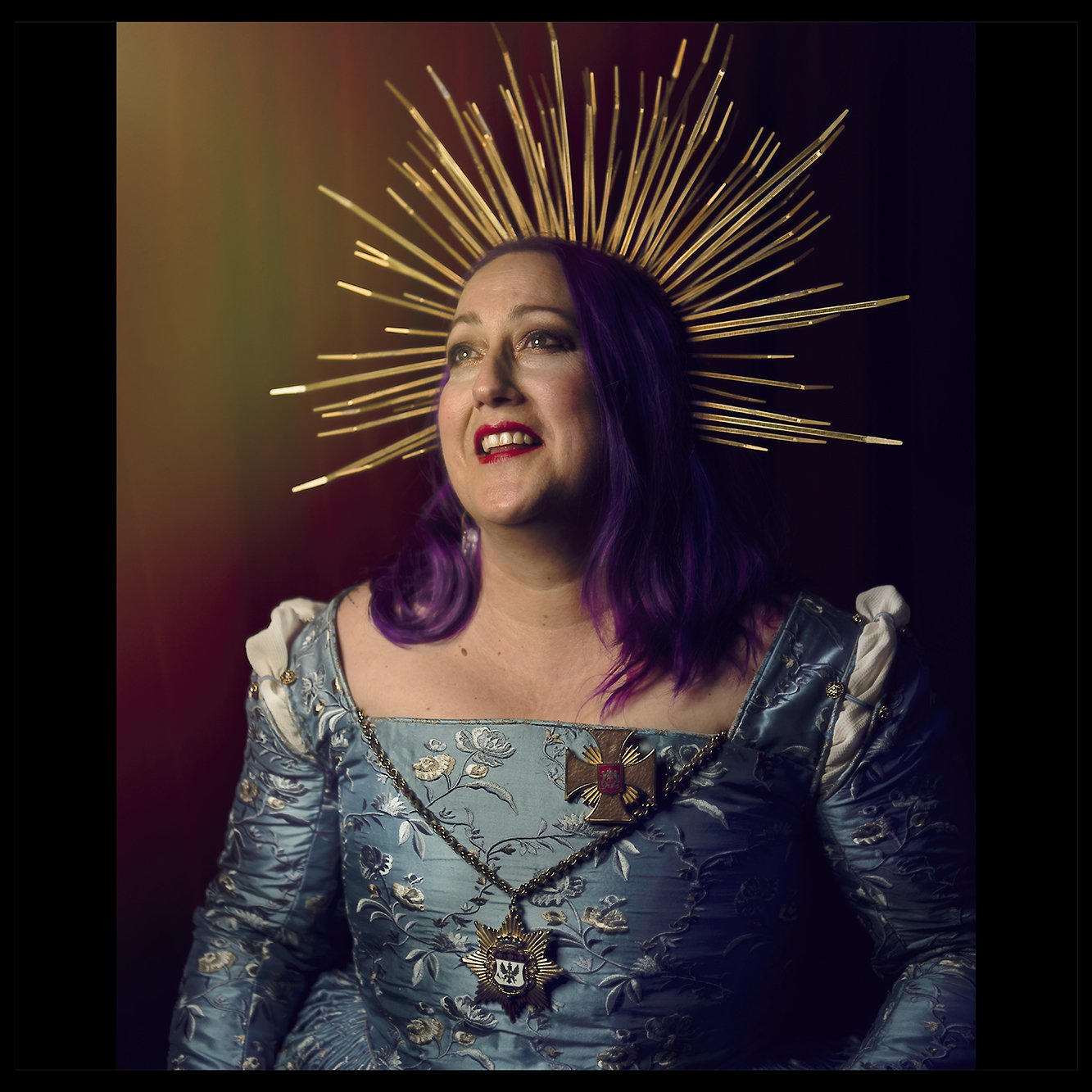 Photo of a woman with a gold crown, purple hair, wearing a blue dress looking off in the distance.