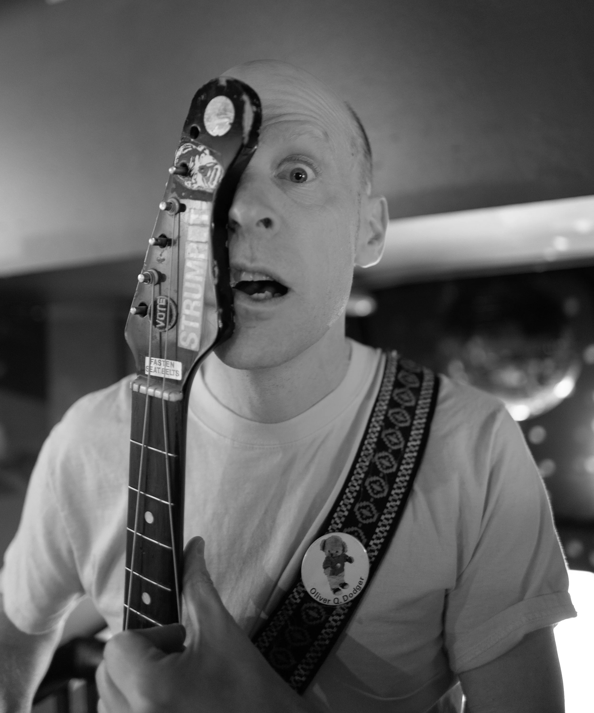 Photo of a man with a white t-shirt and half his face covered by the neck of a guitar in black and white.