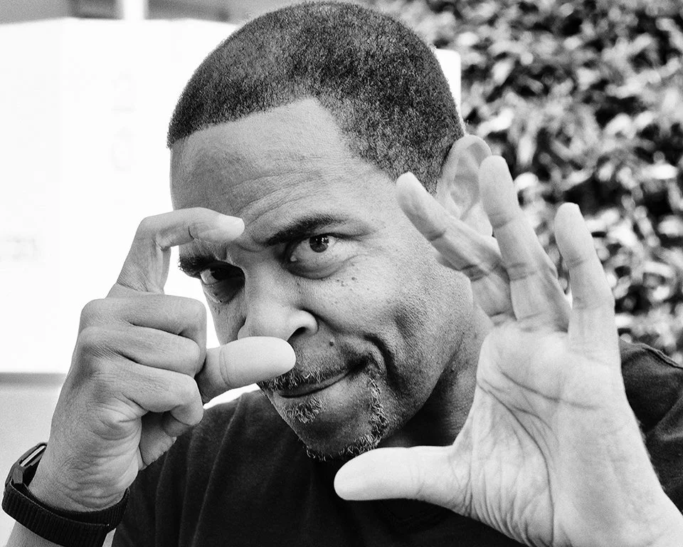 Photo of a man in black and white holding his hands up to simulate taking a photo.
