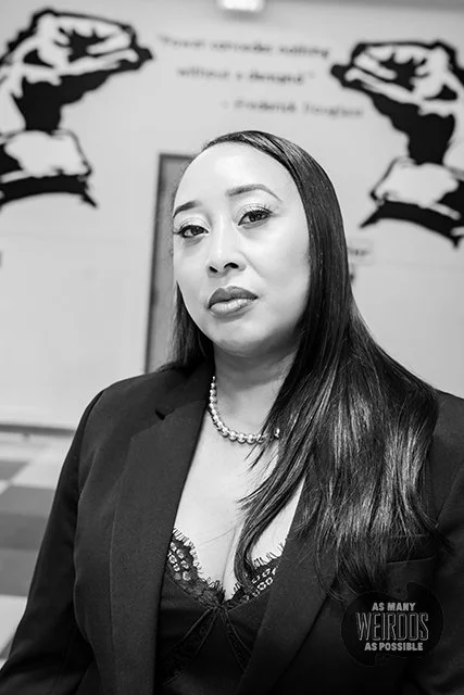 A photo of a woman with long hear, a pearl neckless, and a black jacket looking directly into the camera.