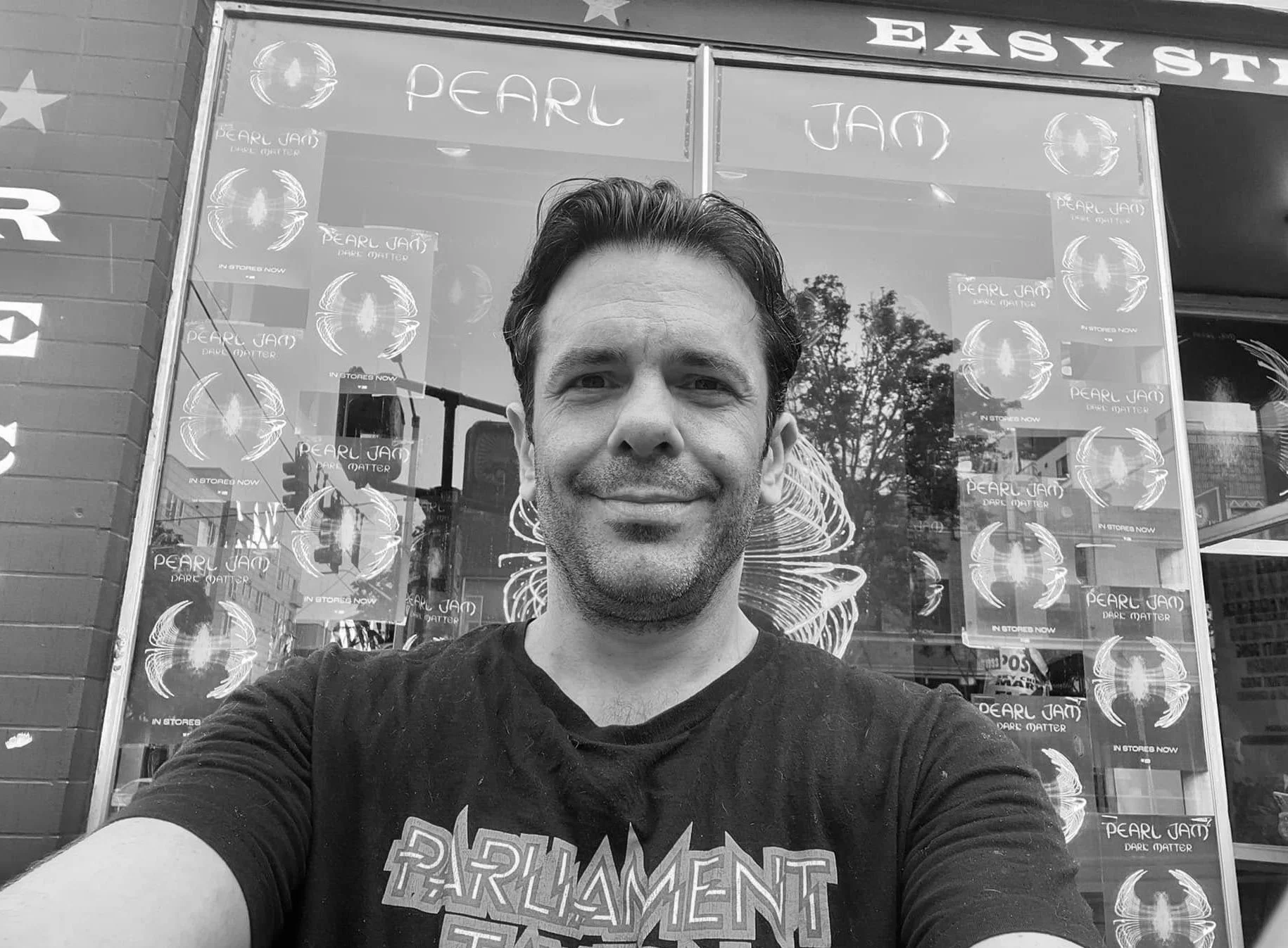 Photo of a man wearing a t-shirt that reads "Parliament" in front of a storefront window.