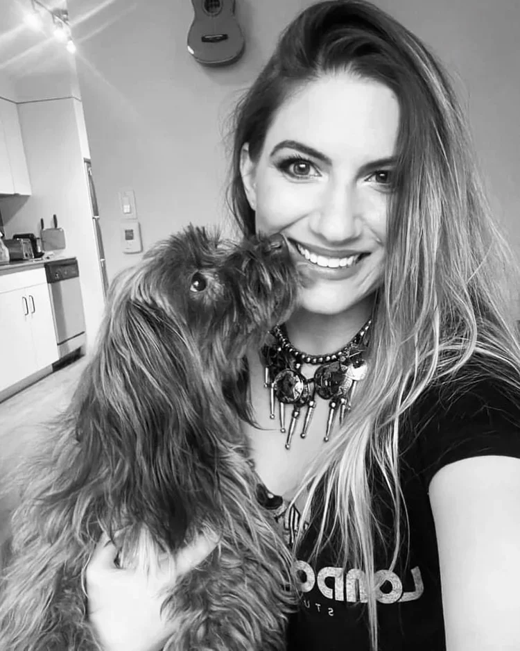 black and white photo of a woman with a neckless and black shirt, holding a dog in her right hand.
