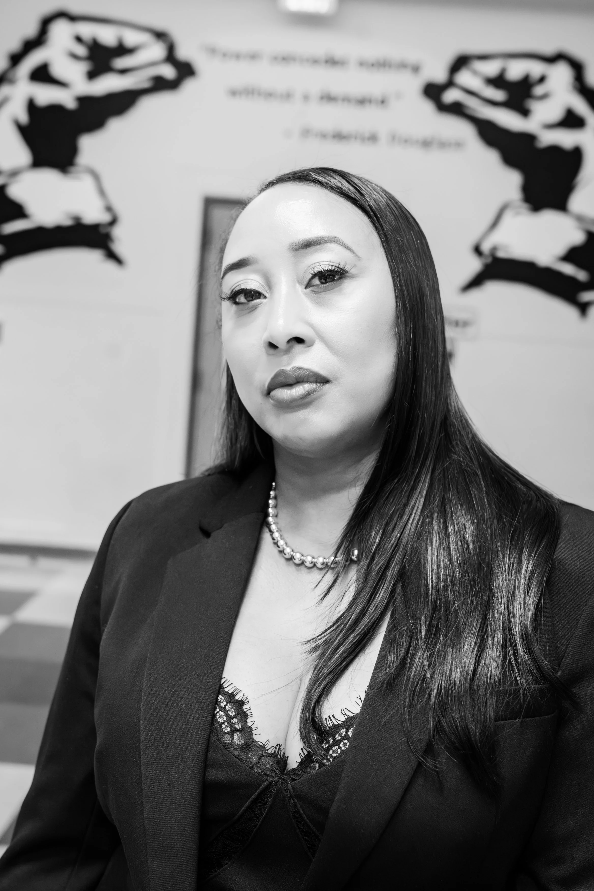 A photo of a woman with long hear, a pearl neckless, and a black jacket looking directly into the camera.