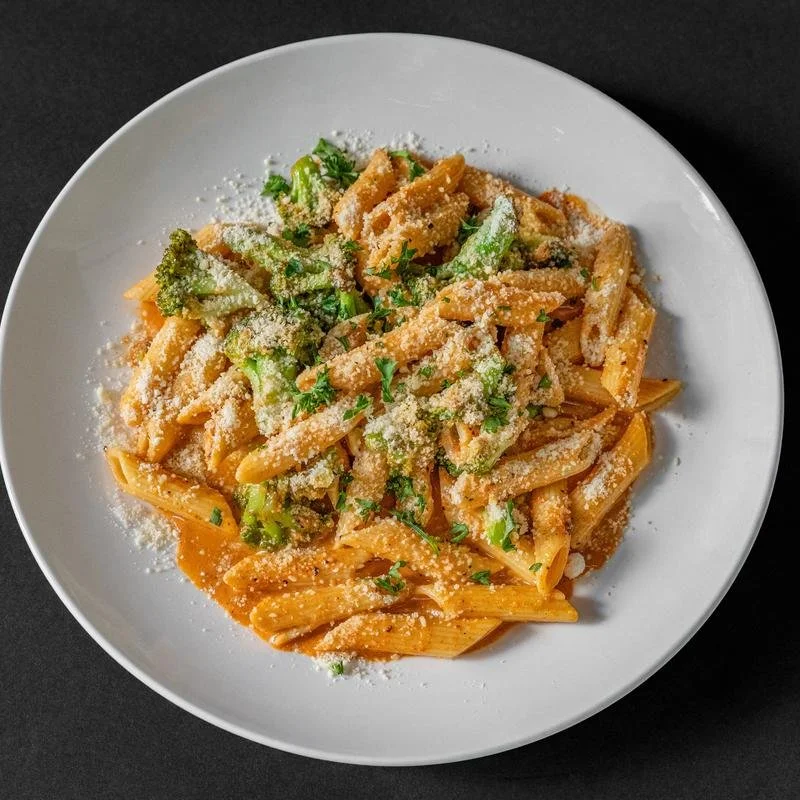 Plate of pasta with broccoli, grated cheese, and herbs on top, served on a white dish against a dark background.