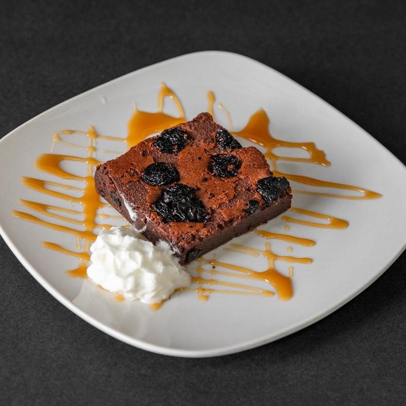 Chocolate brownie with blueberries, caramel drizzle, and whipped cream on a white plate