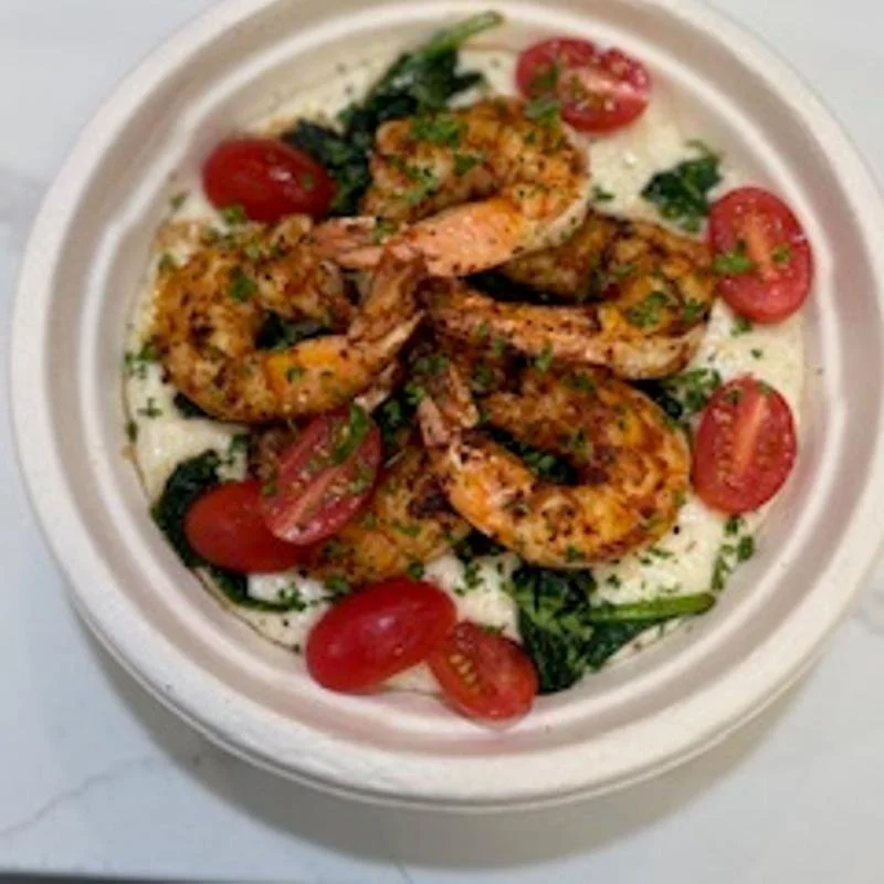 Shrimp and cherry tomato salad on a bed of greens, served in a white bowl.