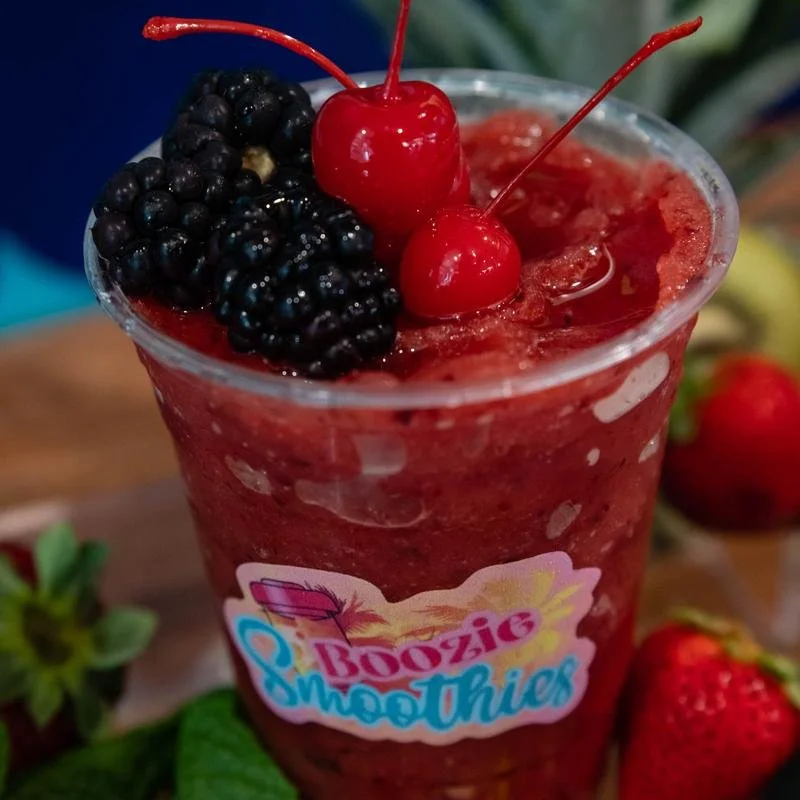 Red berry smoothie with blackberries and cherries on top, in a clear plastic cup with a Boozic Smoothies label.