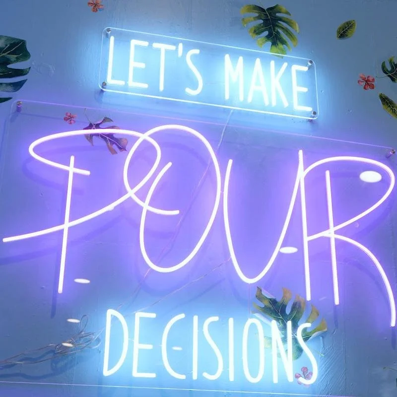 Neon sign with the words "Let's Make Your Tour Decisions" in bright blue and purple colors, decorated with tropical leaves and small flowers.