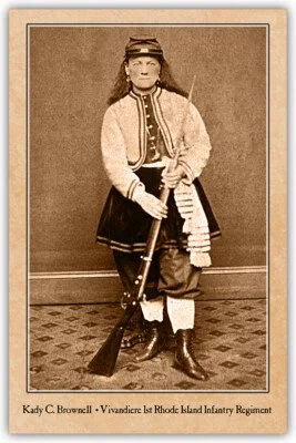 A sepia-toned photograph of a woman in a historical military uniform standing with a rifle, identified as Kady C. Brownell from the Rhode Island Infantry Regiment.