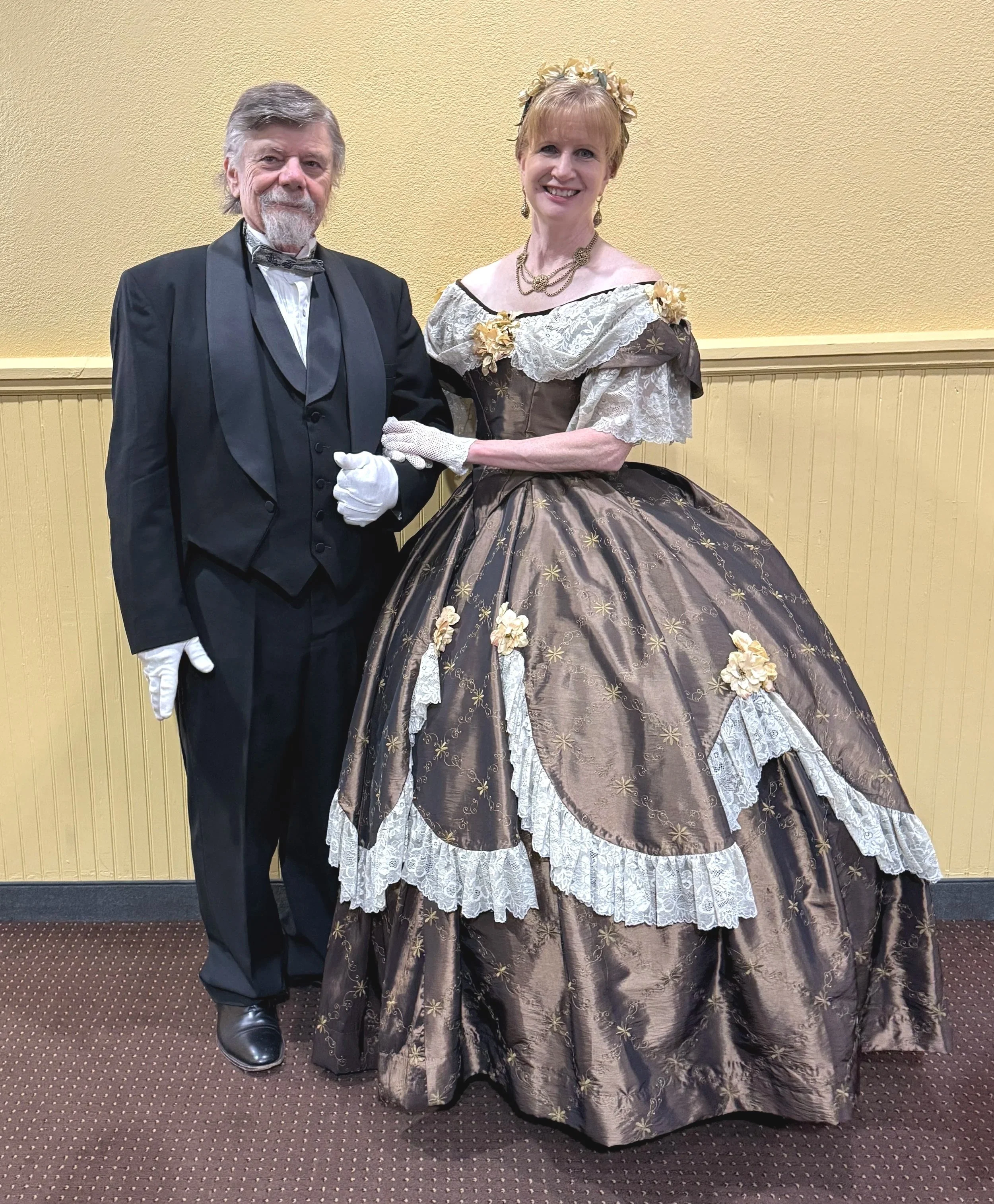 Sharon and Mike Guli dressed in Civil War formal attire as they attend a Civil War Ball in Gettysburg. Mike is wearing a tuxedo with tails and Sharon is wearing a brown ballgown with cream lace and flower trims.