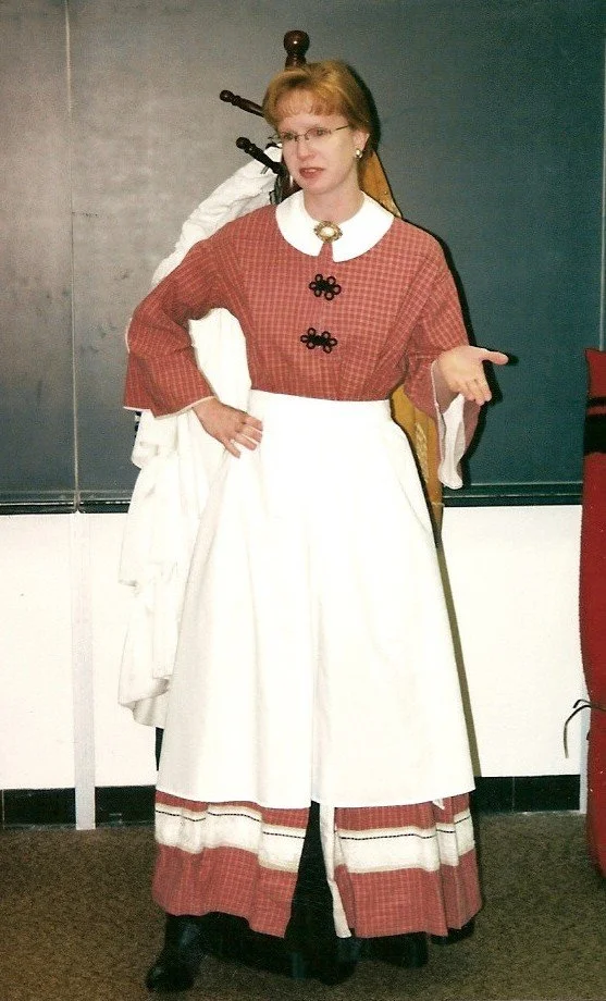 Sharon Guli speaking to a classroom of students while wearing a red Civil War era style dress, known as a wrapper, and apron.