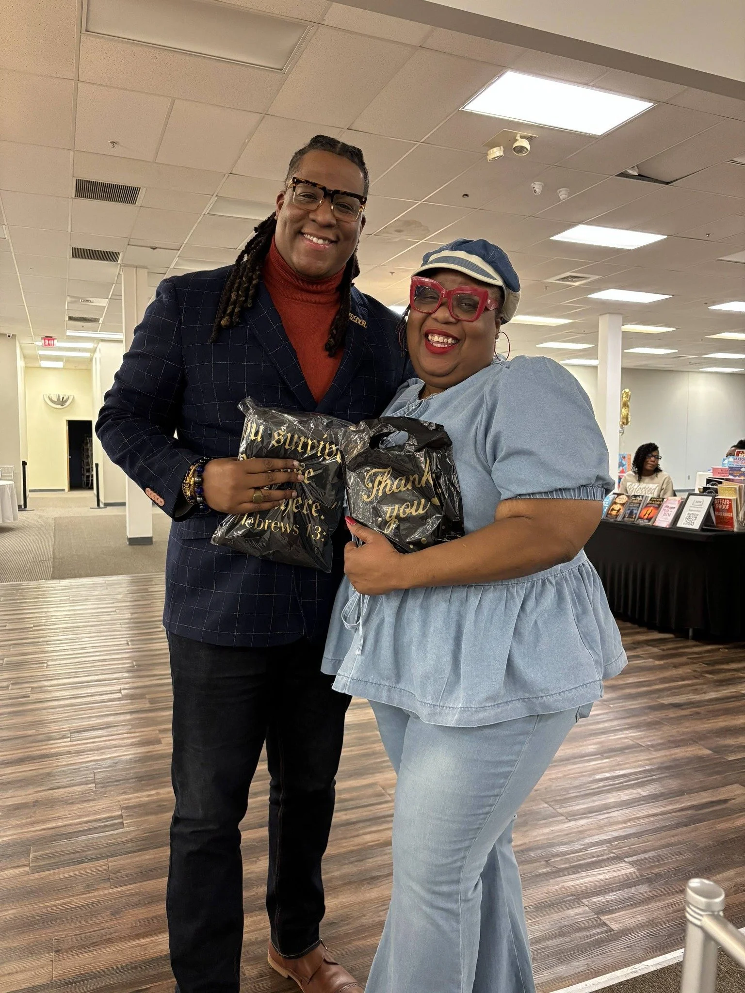 A man and a woman holding gift bags and smiling together in an indoor space.