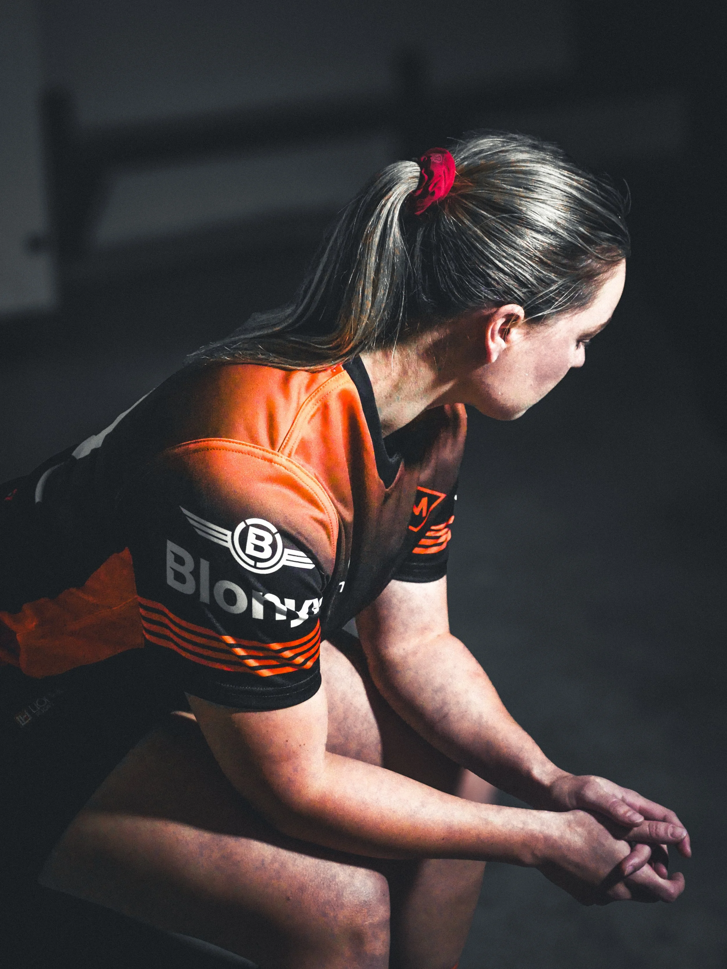 Female athlete in an orange and black sports jersey sitting with hands clasped.