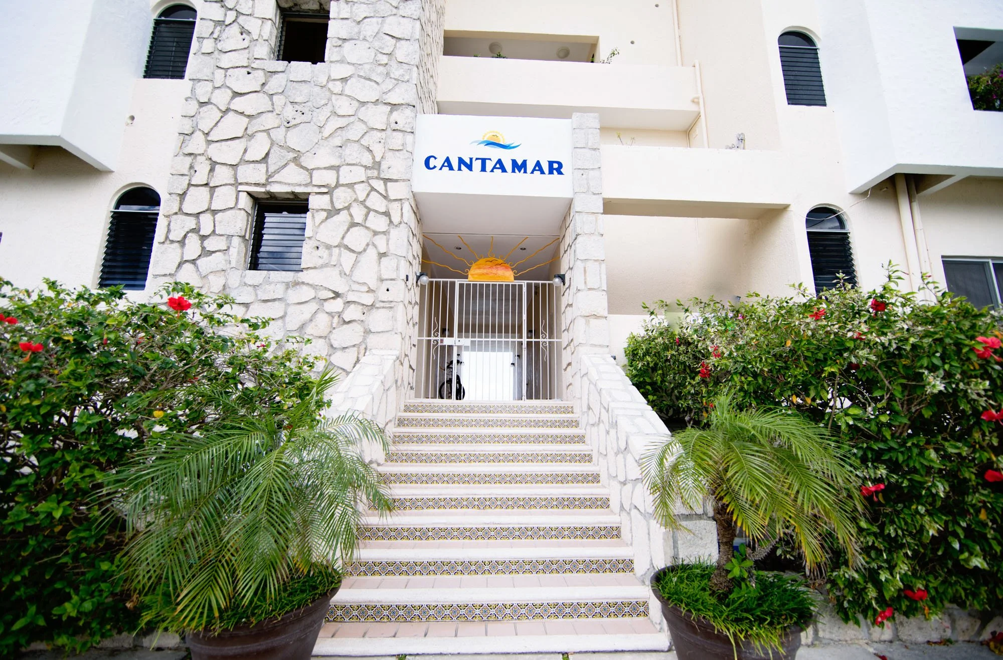Hotel entrance with stairs flanked by potted plants and a sign that says 'CANTAMAR' above the doorway.