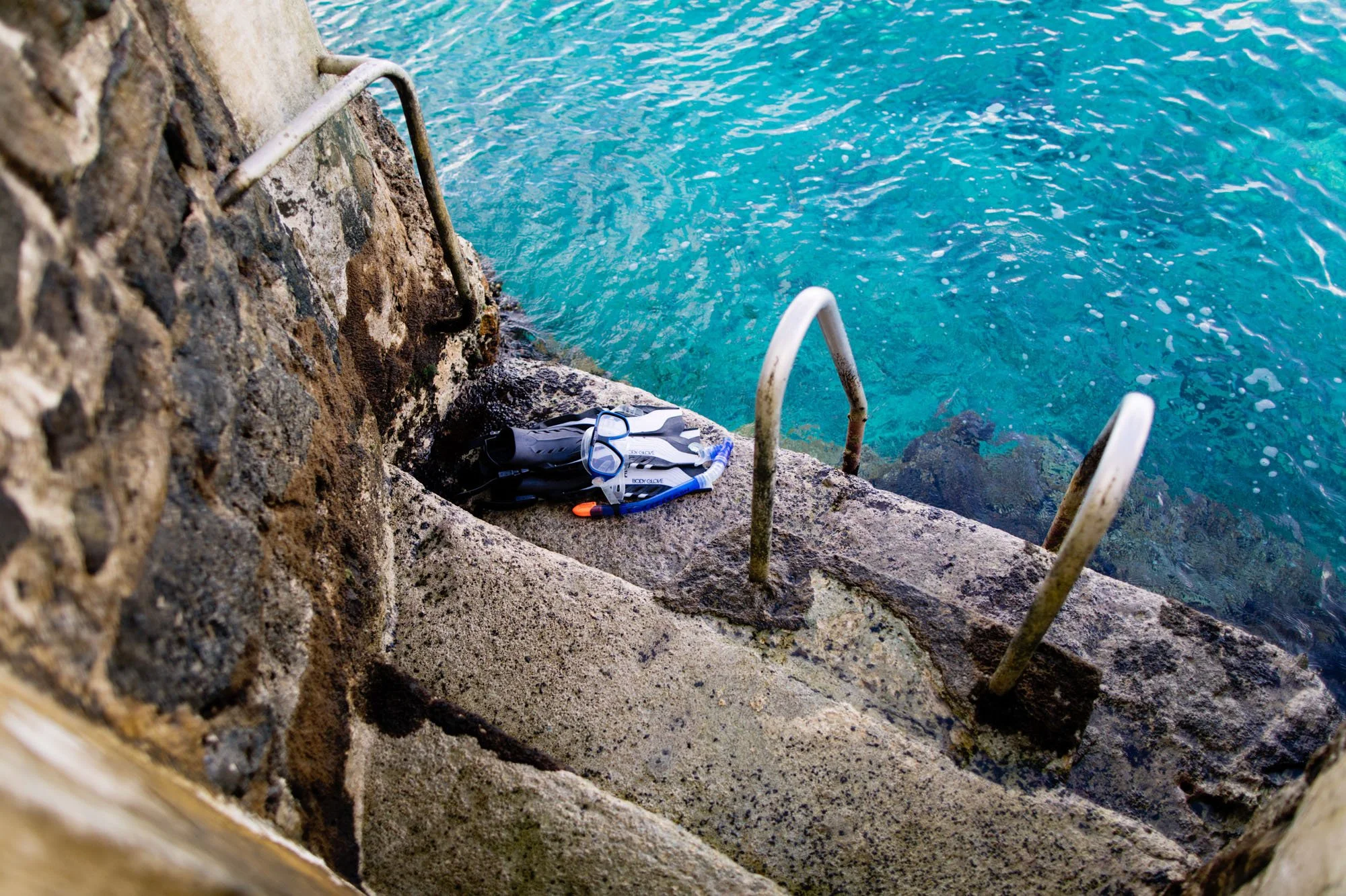 A stone staircase leading into clear blue water, with scuba gear and a snorkel on the steps.