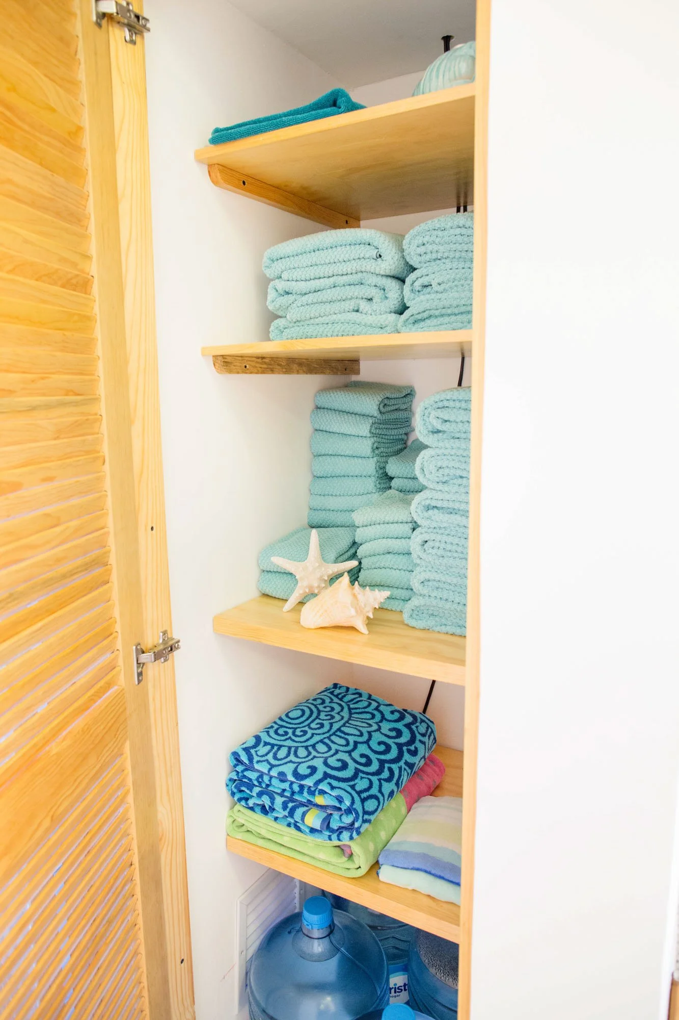 Shelf with folded towels, starfish, shells, and bottled water.