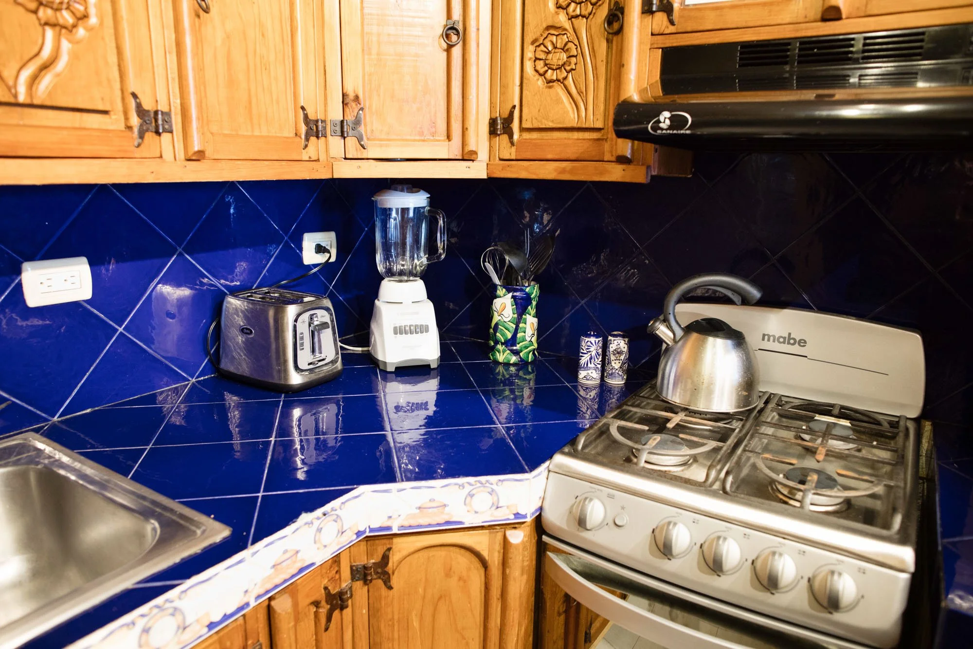 Kitchen countertop with a blender, toaster, utensil holder, and stove with a kettle on top.