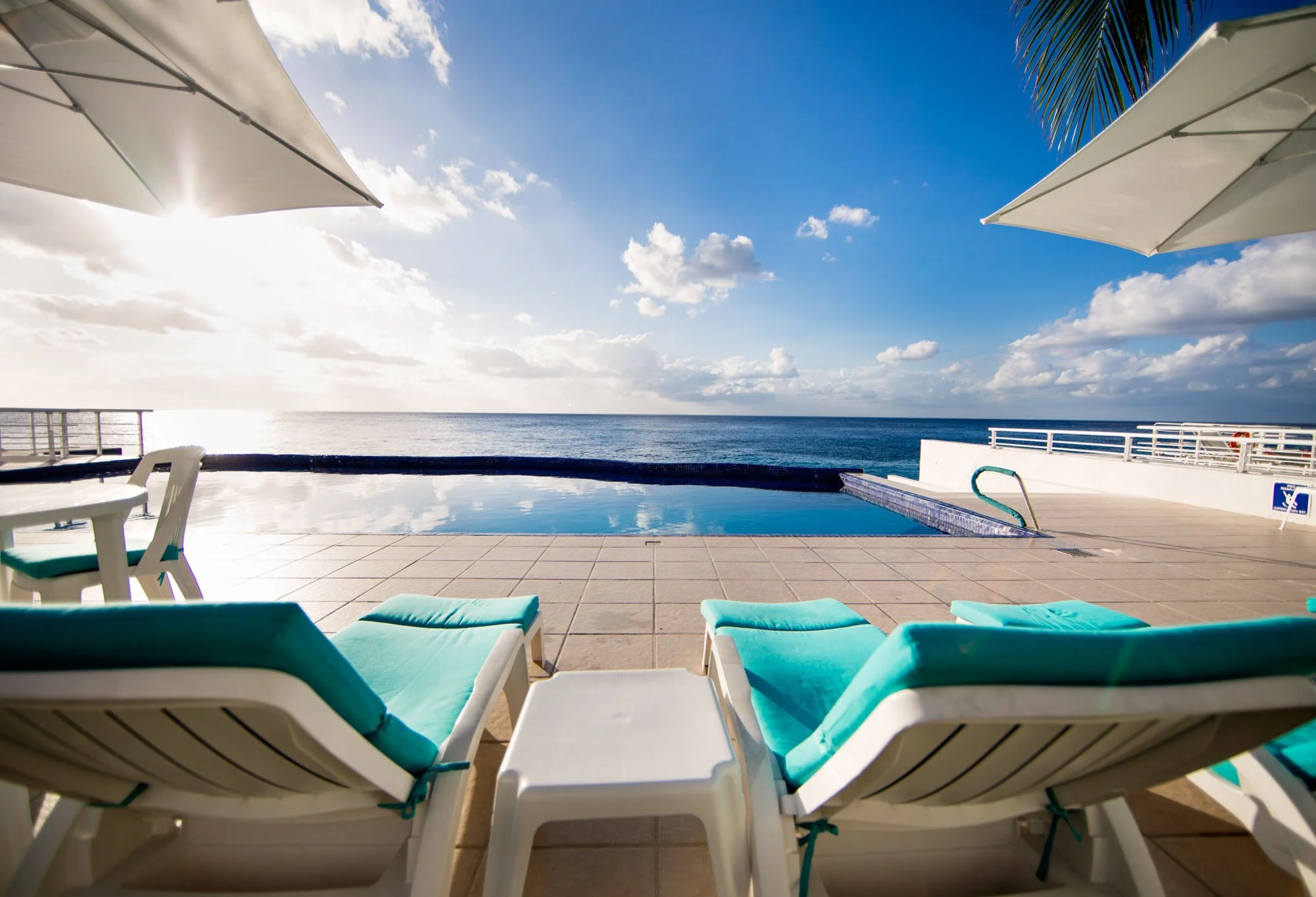 Poolside view with lounge chairs and umbrellas overlooking the ocean on a sunny day.