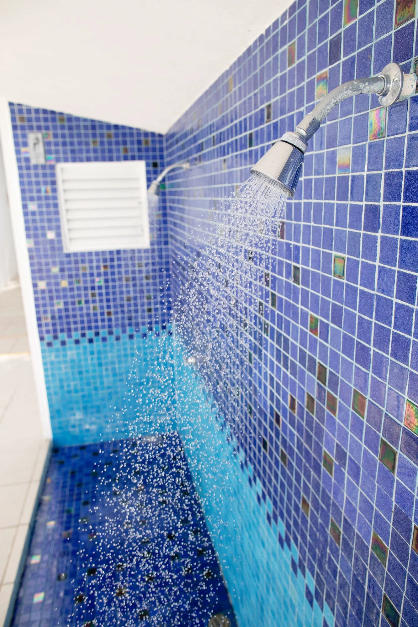 Blue tiled shower area with water spray from a handheld showerhead.