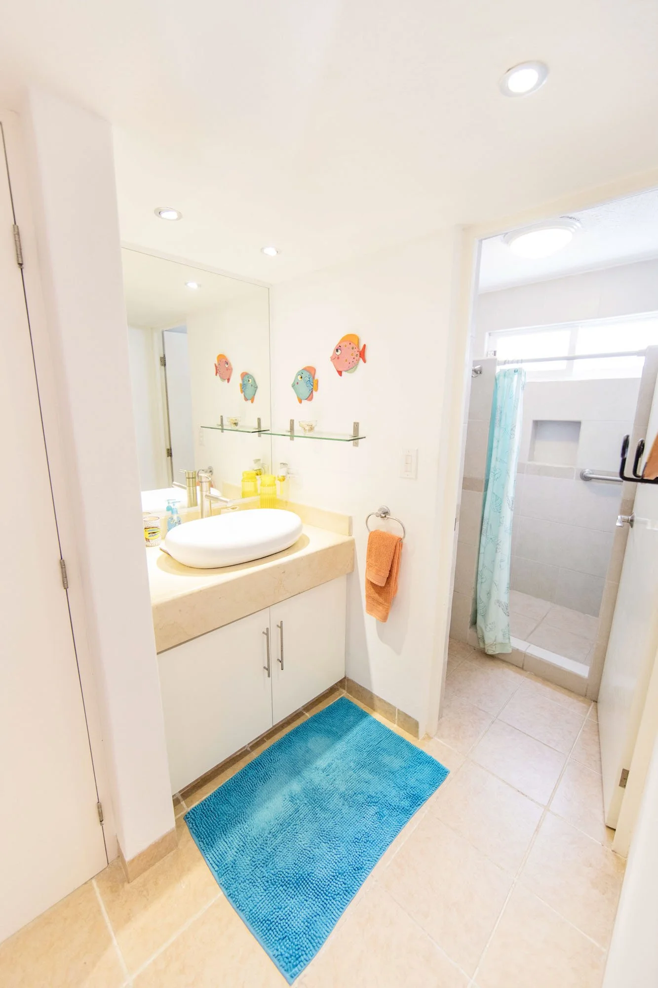 Bathroom with a counter featuring a large white vessel sink, a mirror with colorful fish decorations above, and a walk-in shower with a teal curtain.