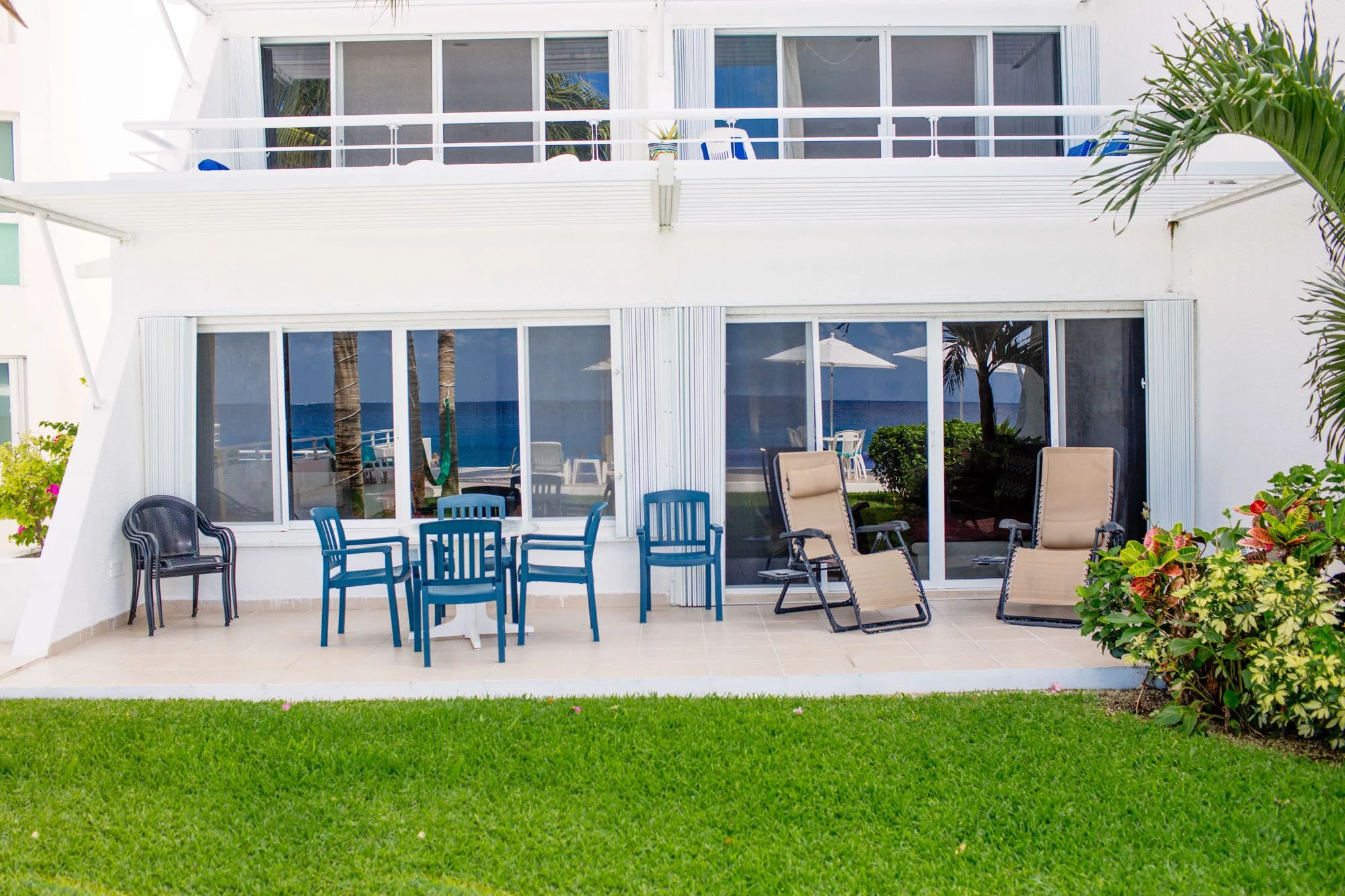 Beachside patio at a Cozumel vacation rental with outdoor furniture, chairs, lounge chairs, and view of the ocean through large glass sliding doors.