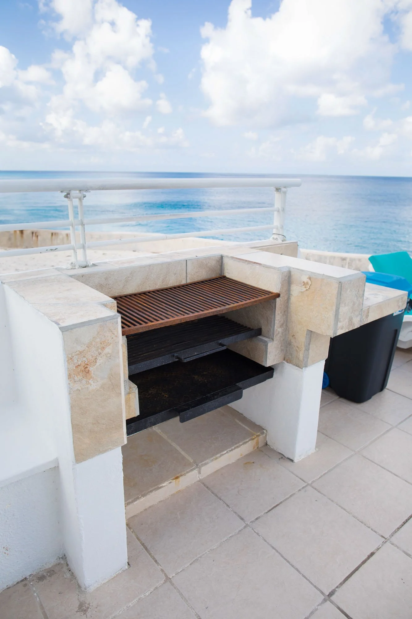 Outdoor balcony with a built-in stone grill and a view of the ocean, partly cloudy sky.