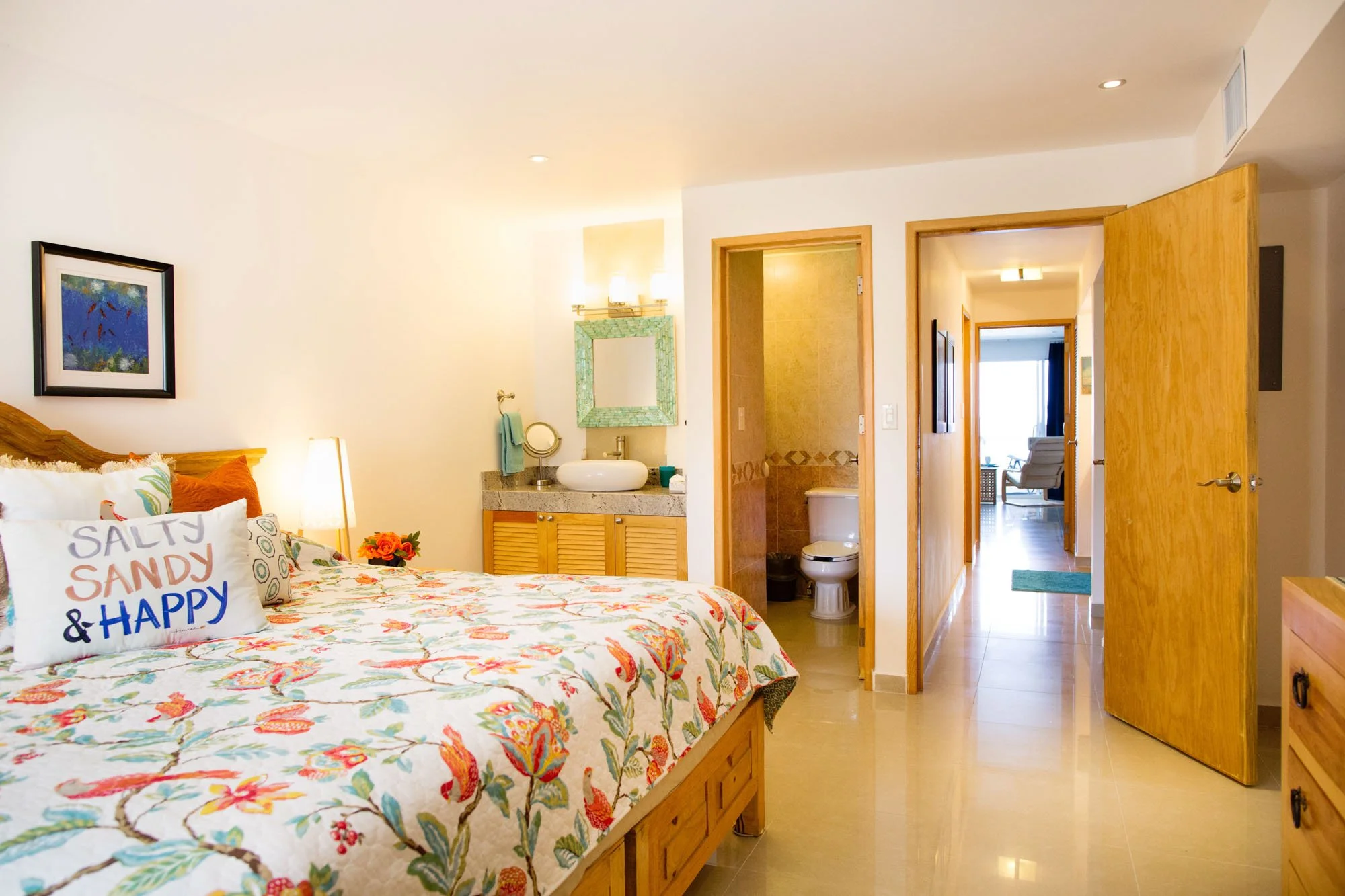  Cozumel vacation rental with a colorful floral bedspread, decorative pillows, a lamp, and a colorful picture on the wall. 