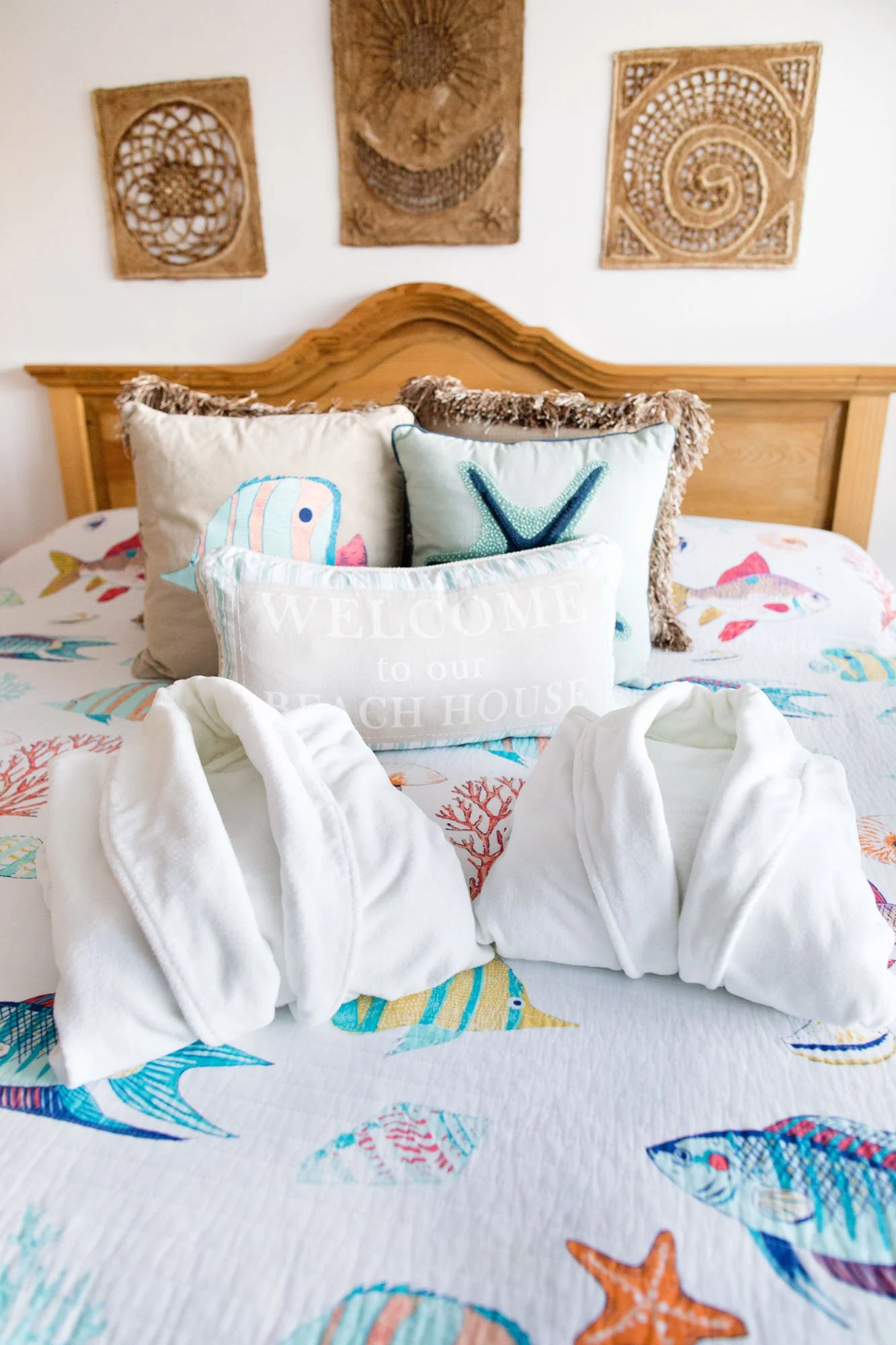 Beach-themed bedroom with a bed decorated with pillows featuring fish and coral patterns, two white towel swans, and ocean-themed wall art.