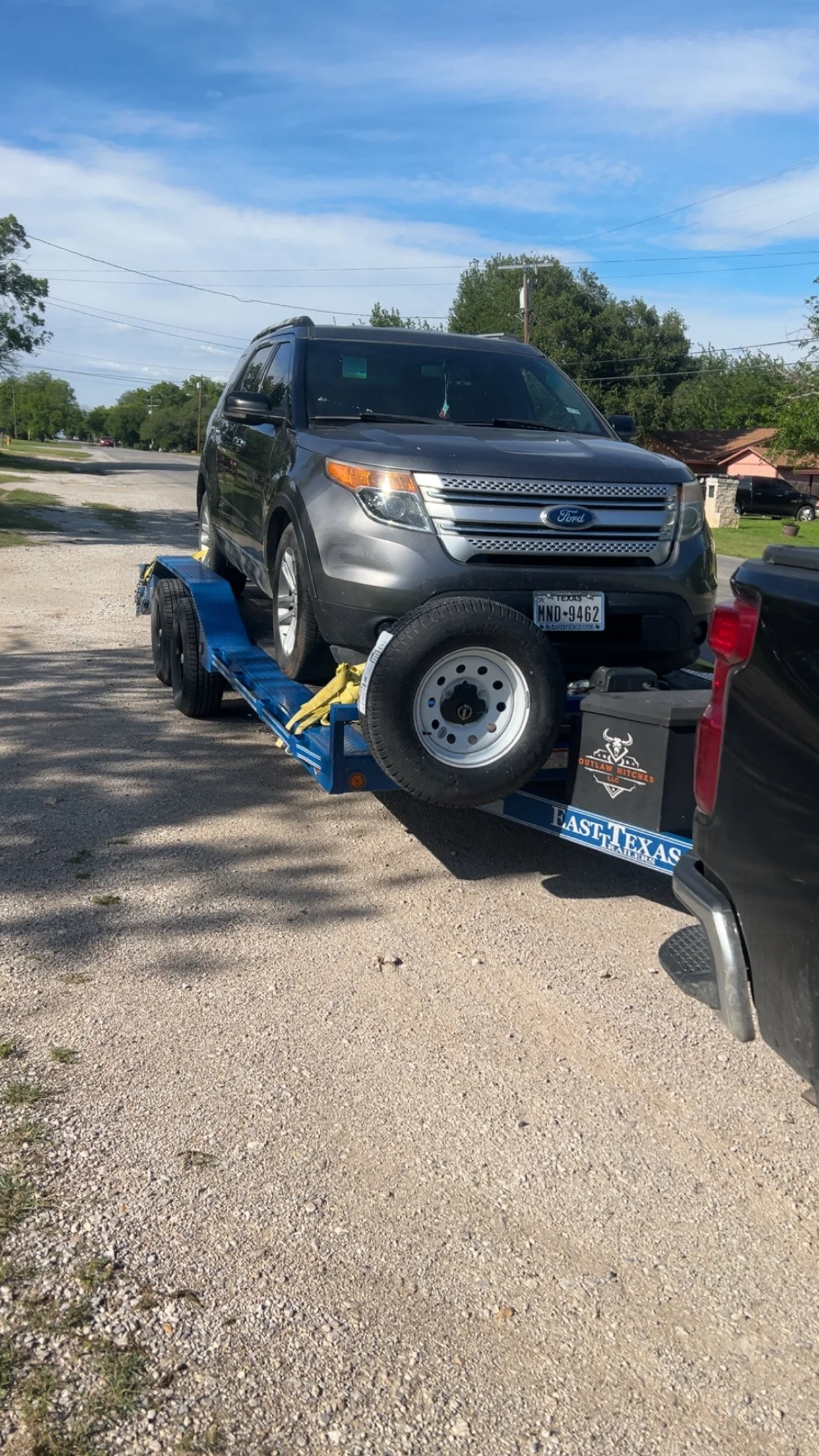 A black vehicle on a blue flatbed tow truck parked on a dirt lot.