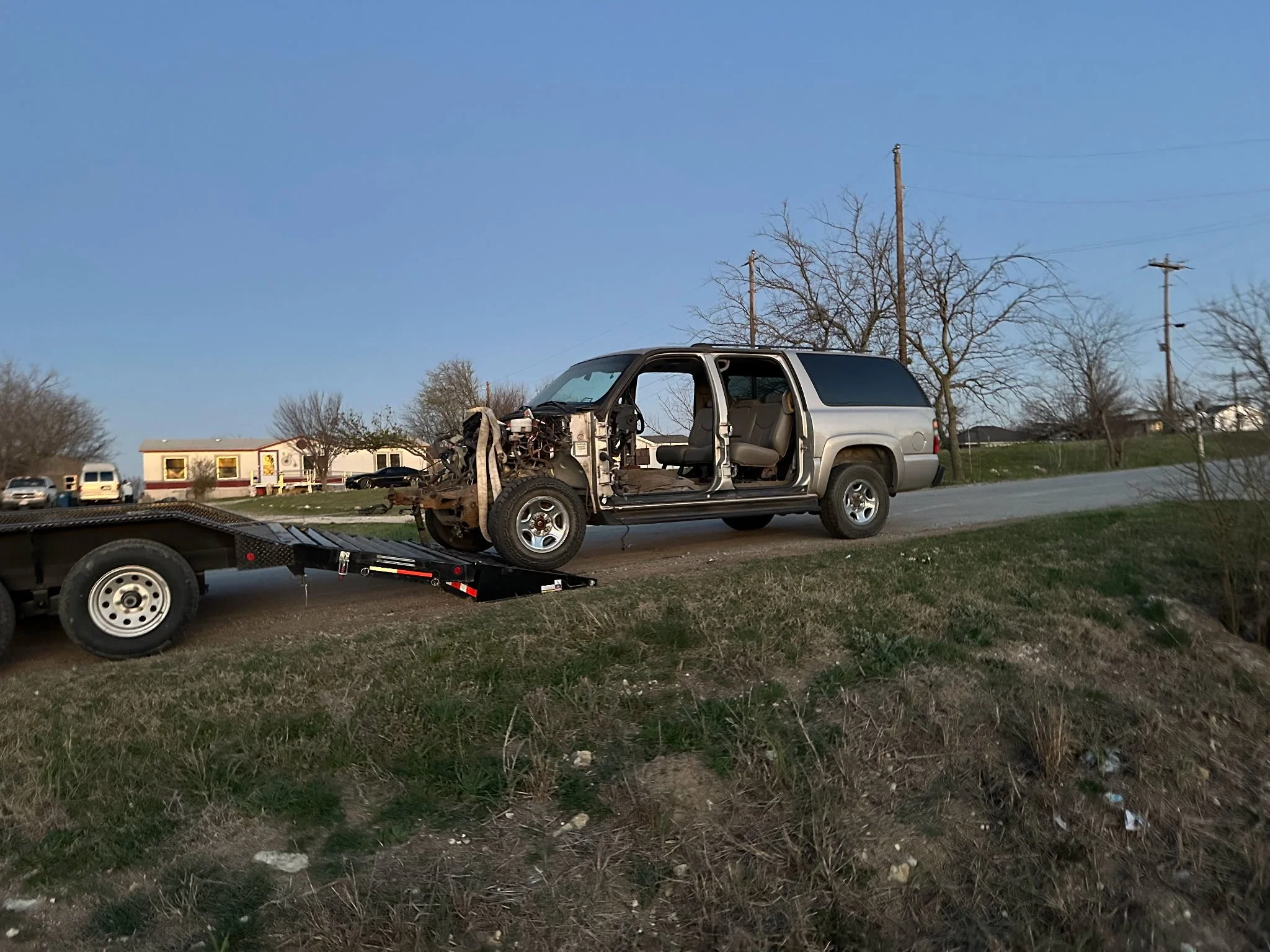 A damaged silver SUV with the front end completely destroyed is being loaded onto a flatbed tow truck on a rural road.