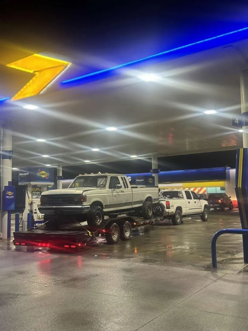 A white pickup truck being transported on a flatbed trailer.