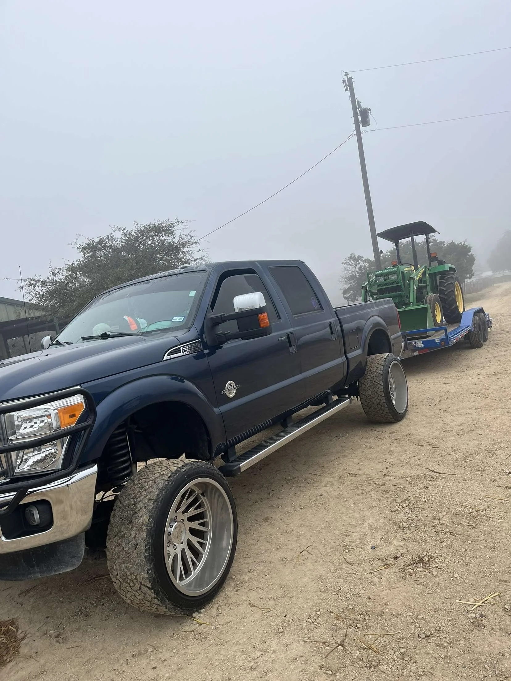 A black pickup truck hauling a trailer with a green tractor on it.