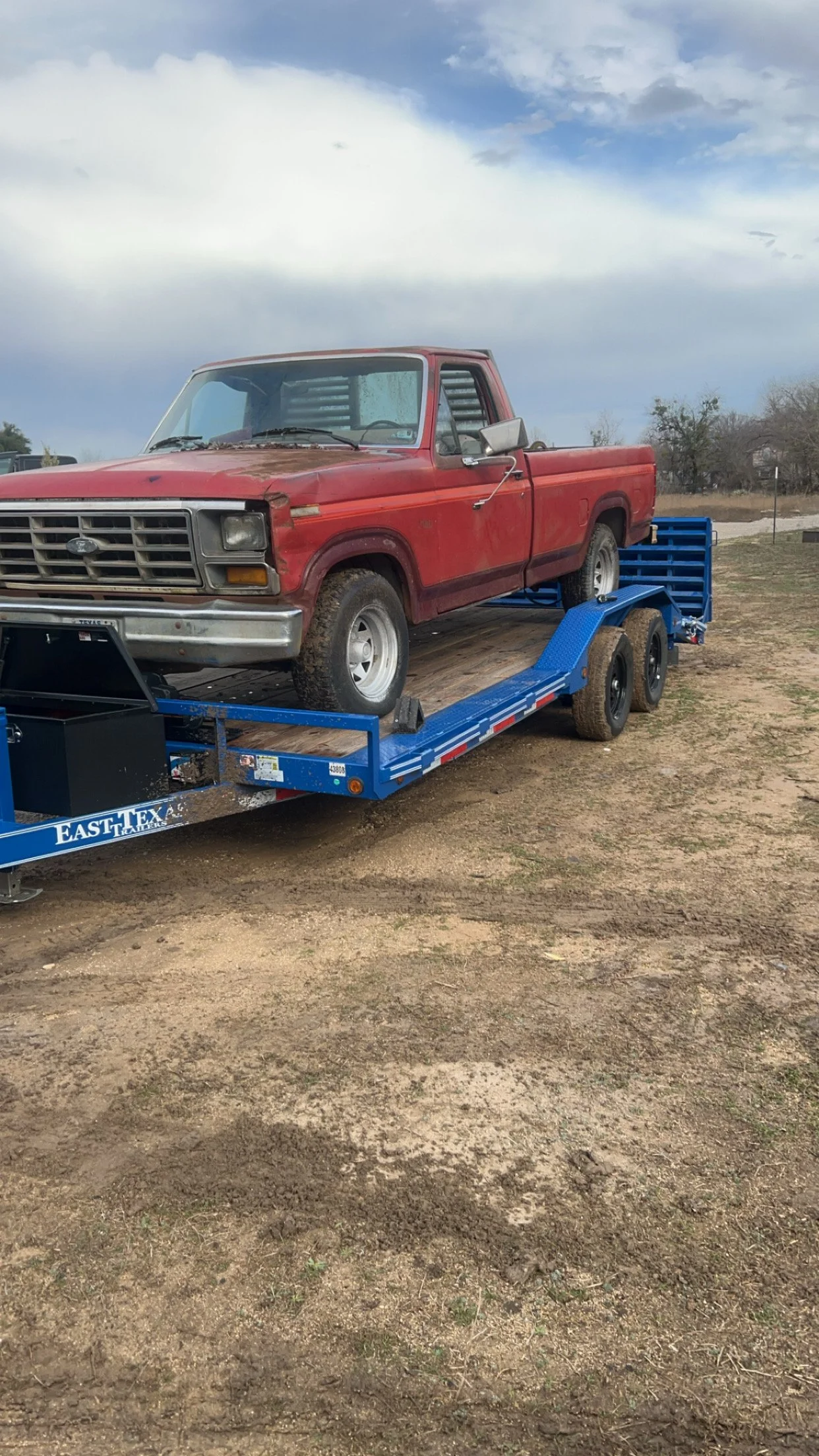 Old red pickup truck on a blue flatbed trailer.