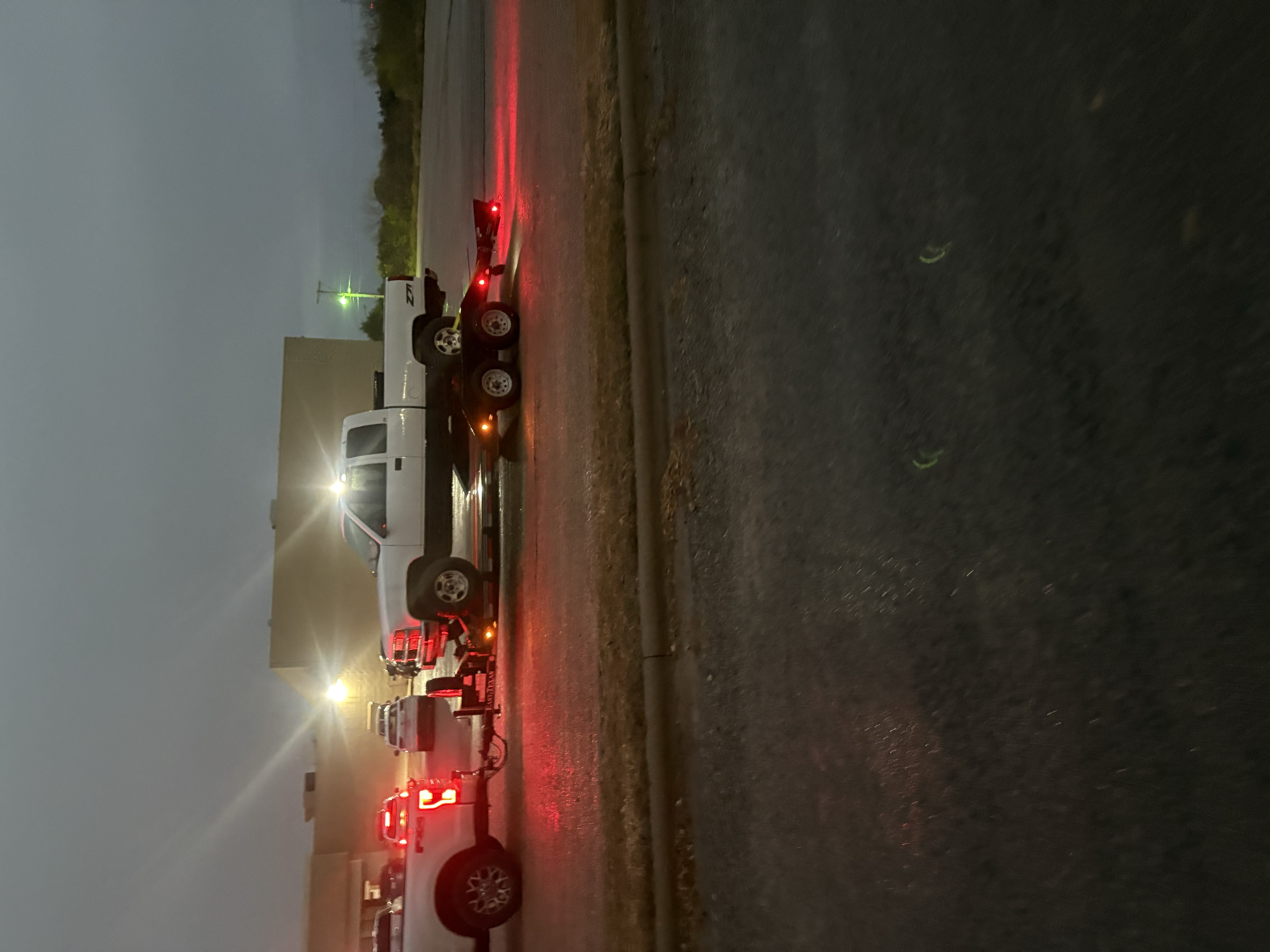 A white pickup truck being towed on a flatbed trailer by a black semi-truck at night.