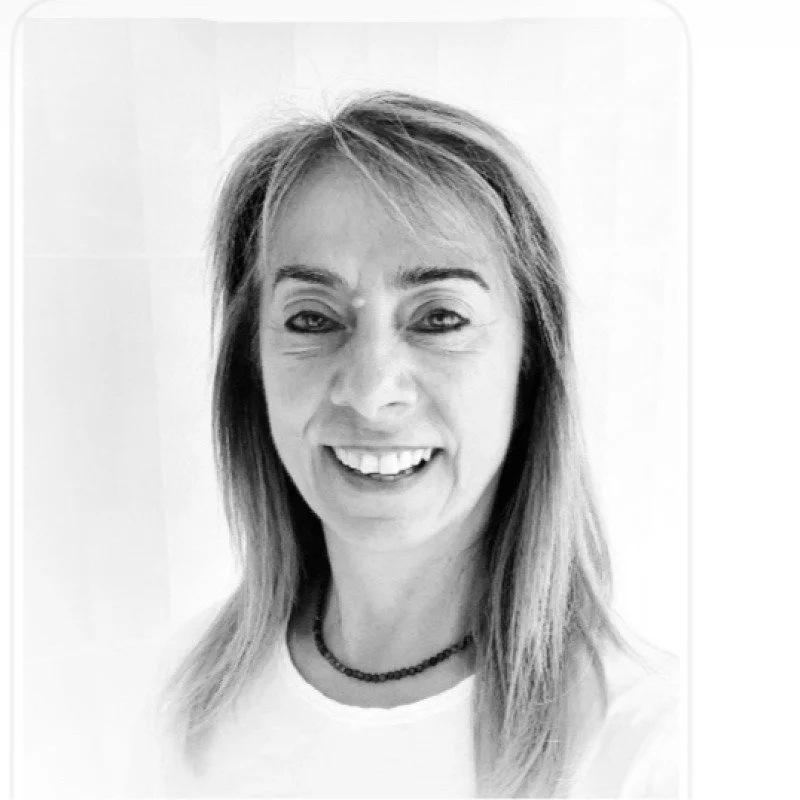 Black and white photo of a smiling woman with shoulder-length hair, wearing a beaded necklace and a white top.