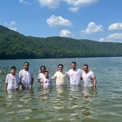 Seven people standing in a lake with hills and a partly cloudy sky in the background.