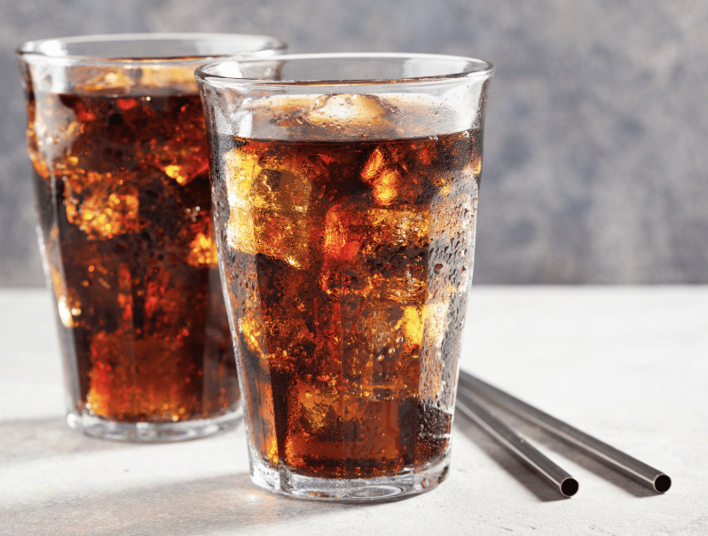 Two glasses of cola with ice cubes, condensation on glasses, and metal straws on a light surface with a gray background.