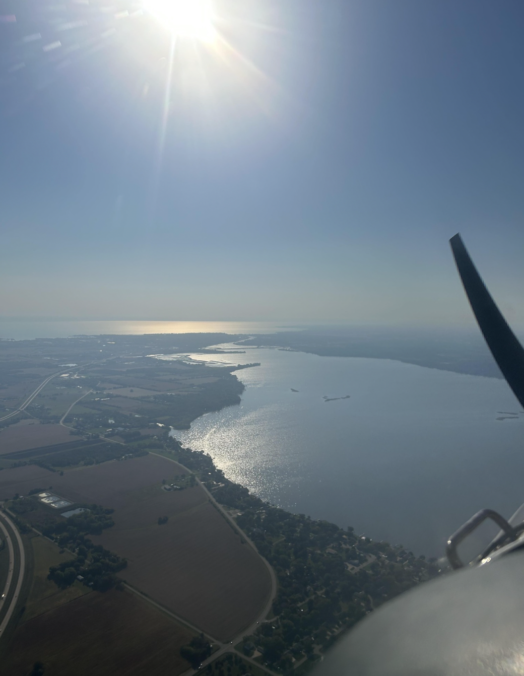Aerial view of a large lake with surrounding land, taken from an airplane with the sun shining brightly in clear sky.