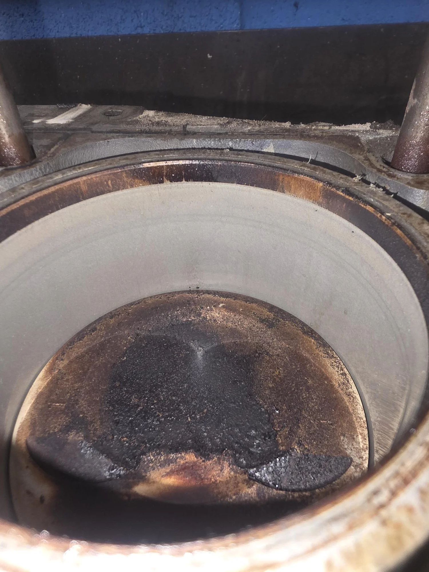 Detailed forensic view of oil-saturated carbon deposits on a Porsche 944 piston; verifying zero cylinder wall scoring before pressurized ring-land purge.