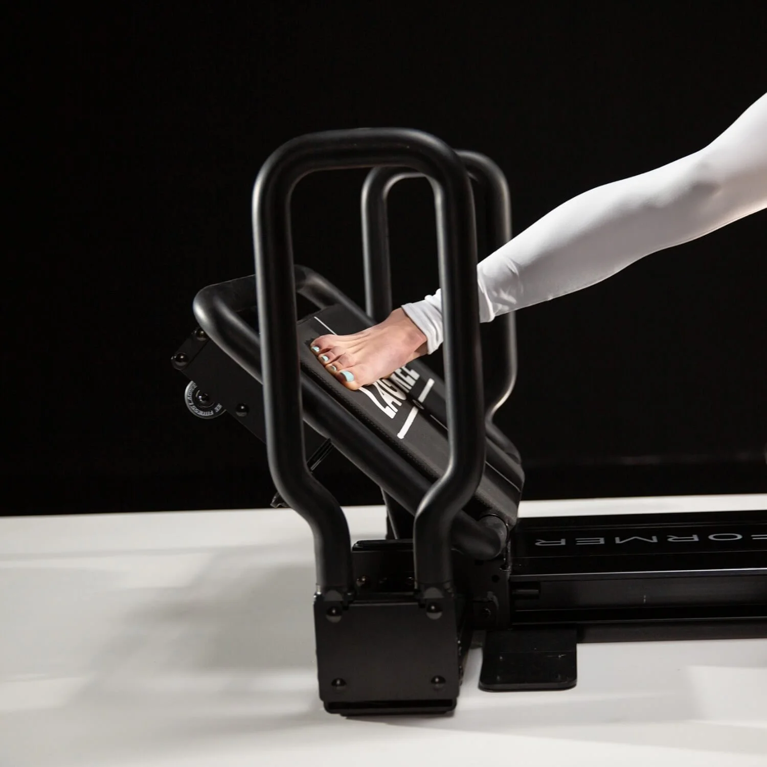 Woman using a Lagree Mini Pro reformer machine for Pilates exercises in a dark studio