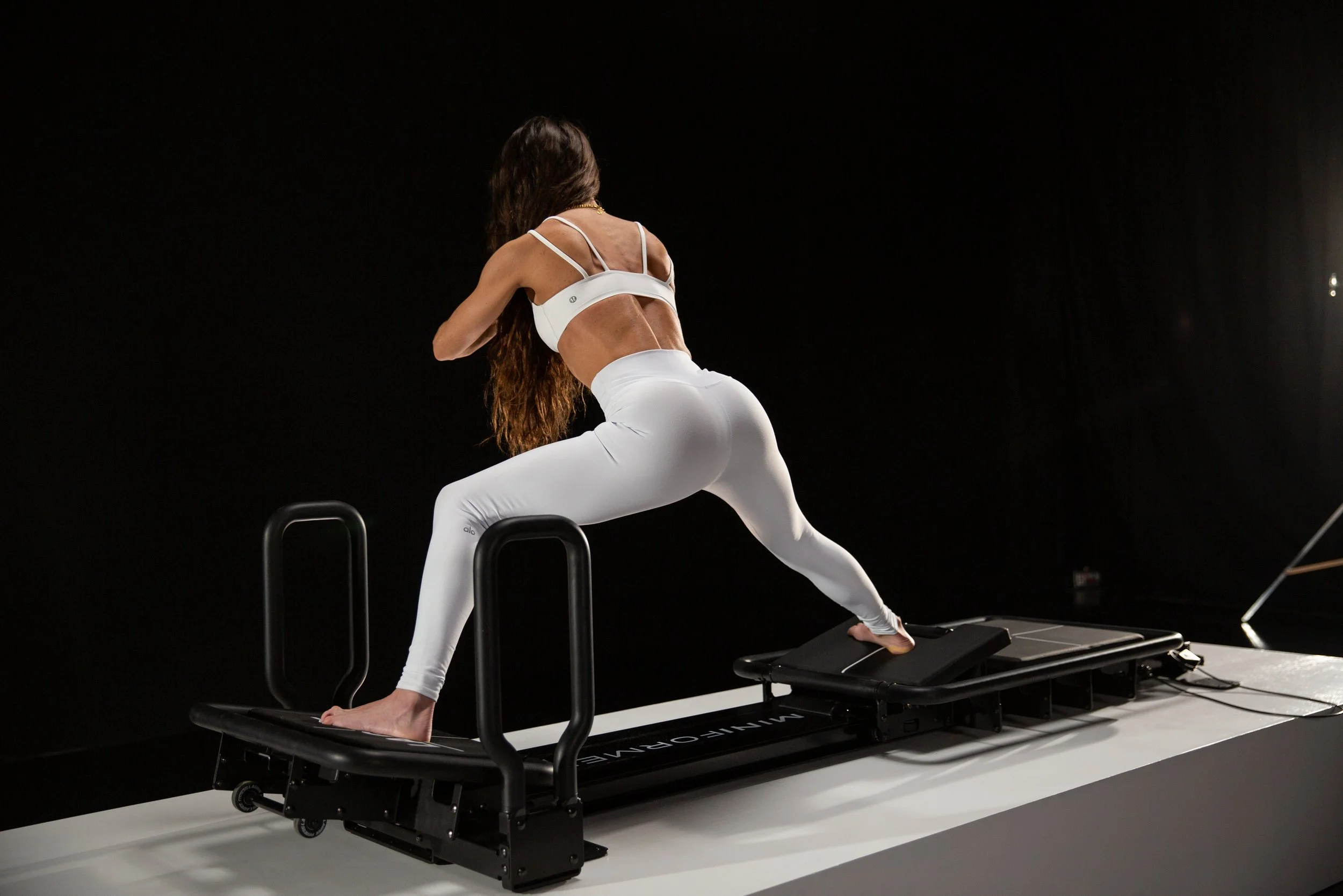 Woman using a Lagree Mini Pro reformer machine for Pilates exercises in a dark studio