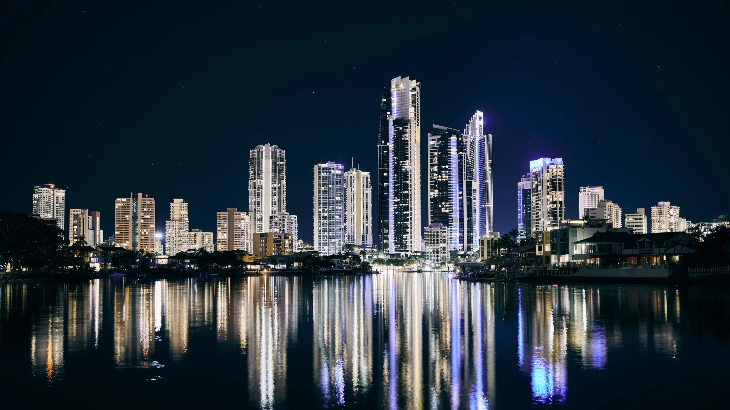 Nighttime city skyline with tall illuminated skyscrapers reflected in water