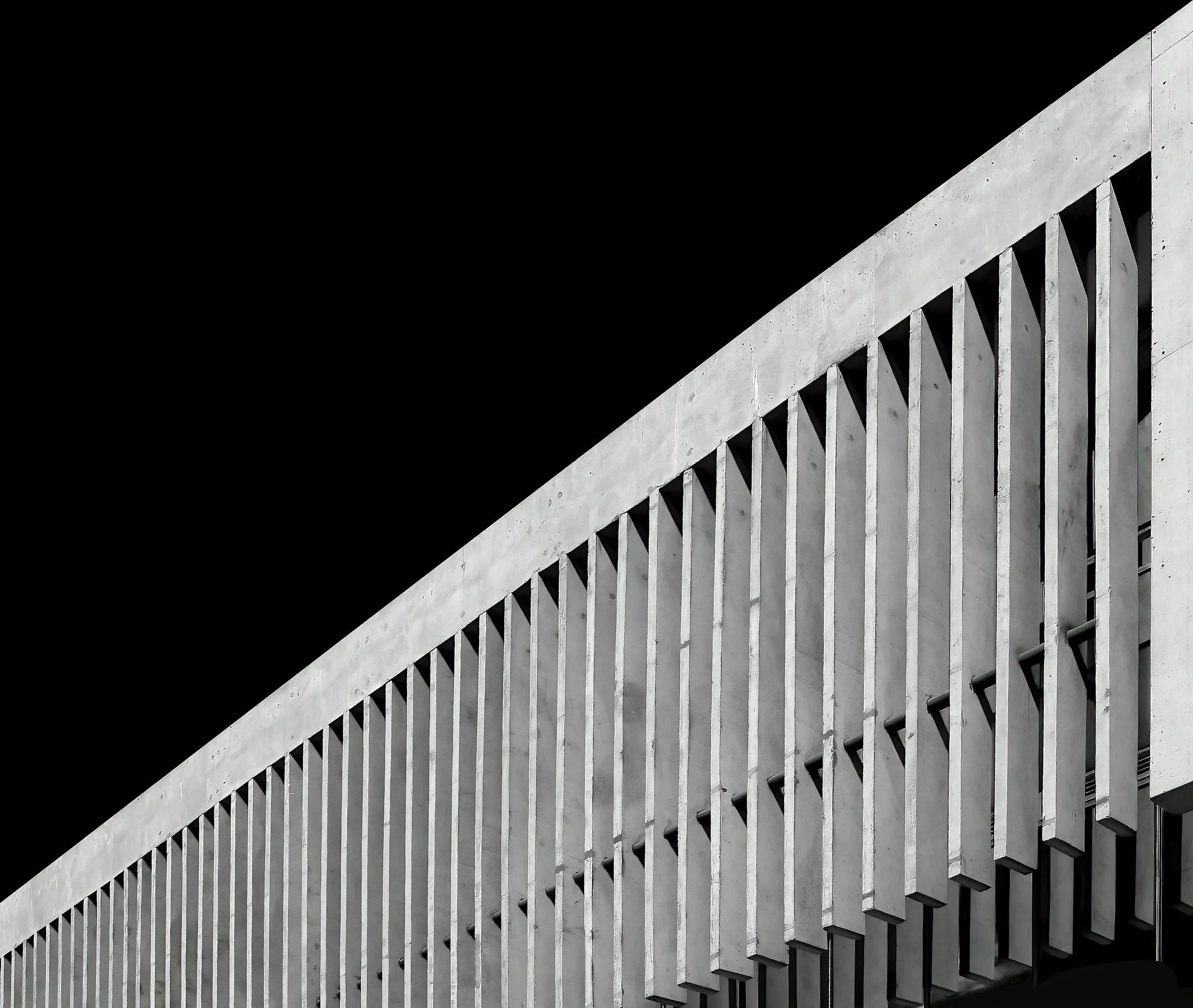Close-up of a modern concrete building with vertical slats and a dark sky.