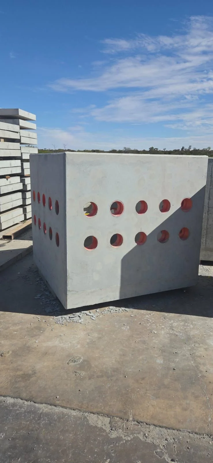 A large concrete block with circular holes in a construction site under a blue sky with some clouds.