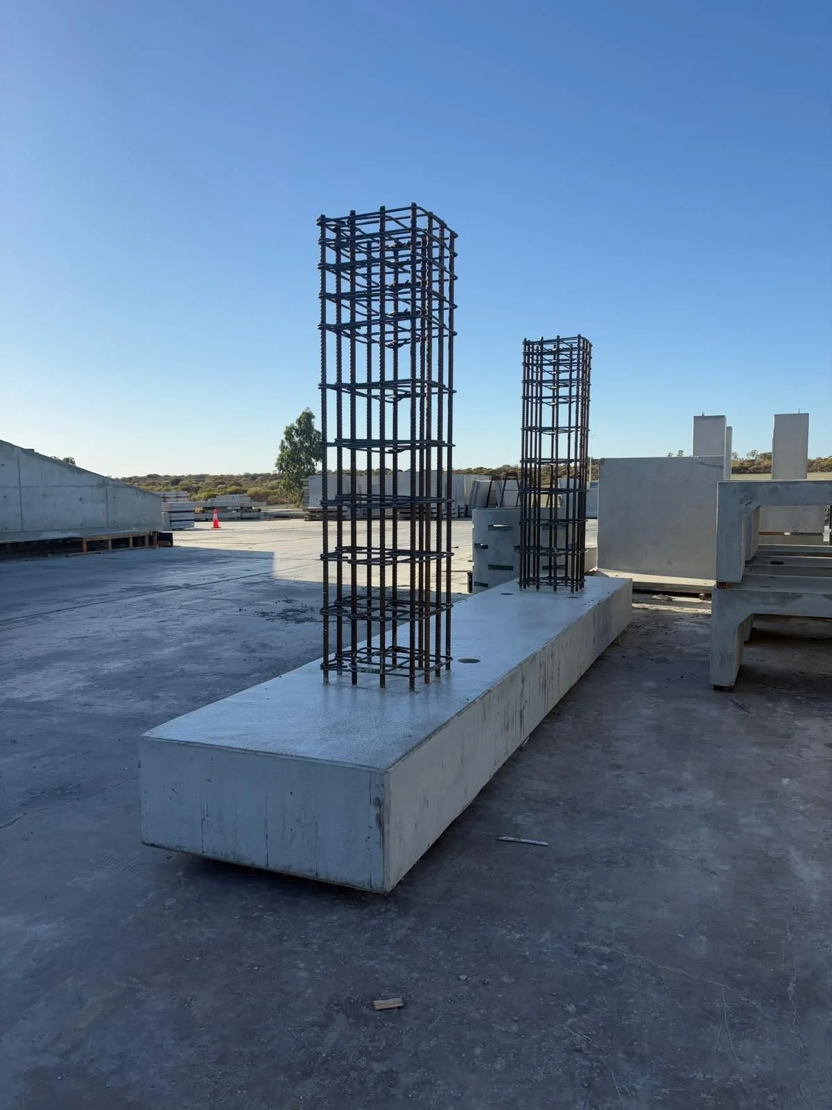 Construction site with two tall steel rebar structures on a large concrete base under a clear blue sky.