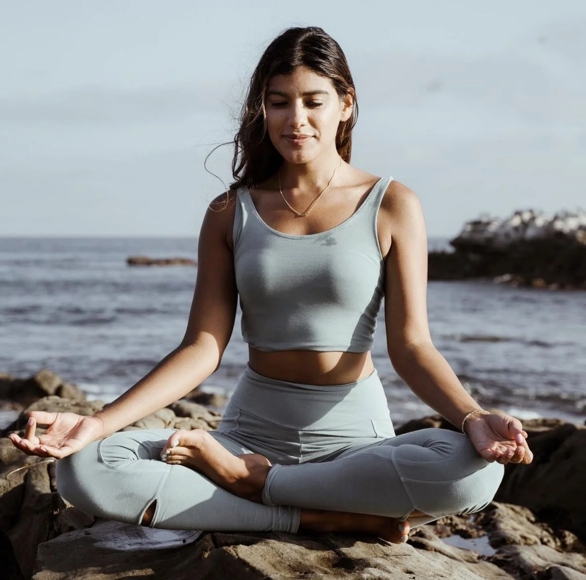 A young woman practicing yoga or meditation on the beach during daytime.