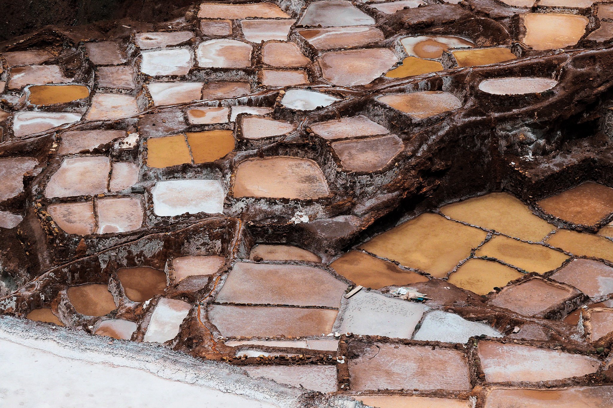 Maras, Peru: Close-up of a stone pathway with irregularly shaped stones, some filled with water or salt, bordered by rough dark mortar.