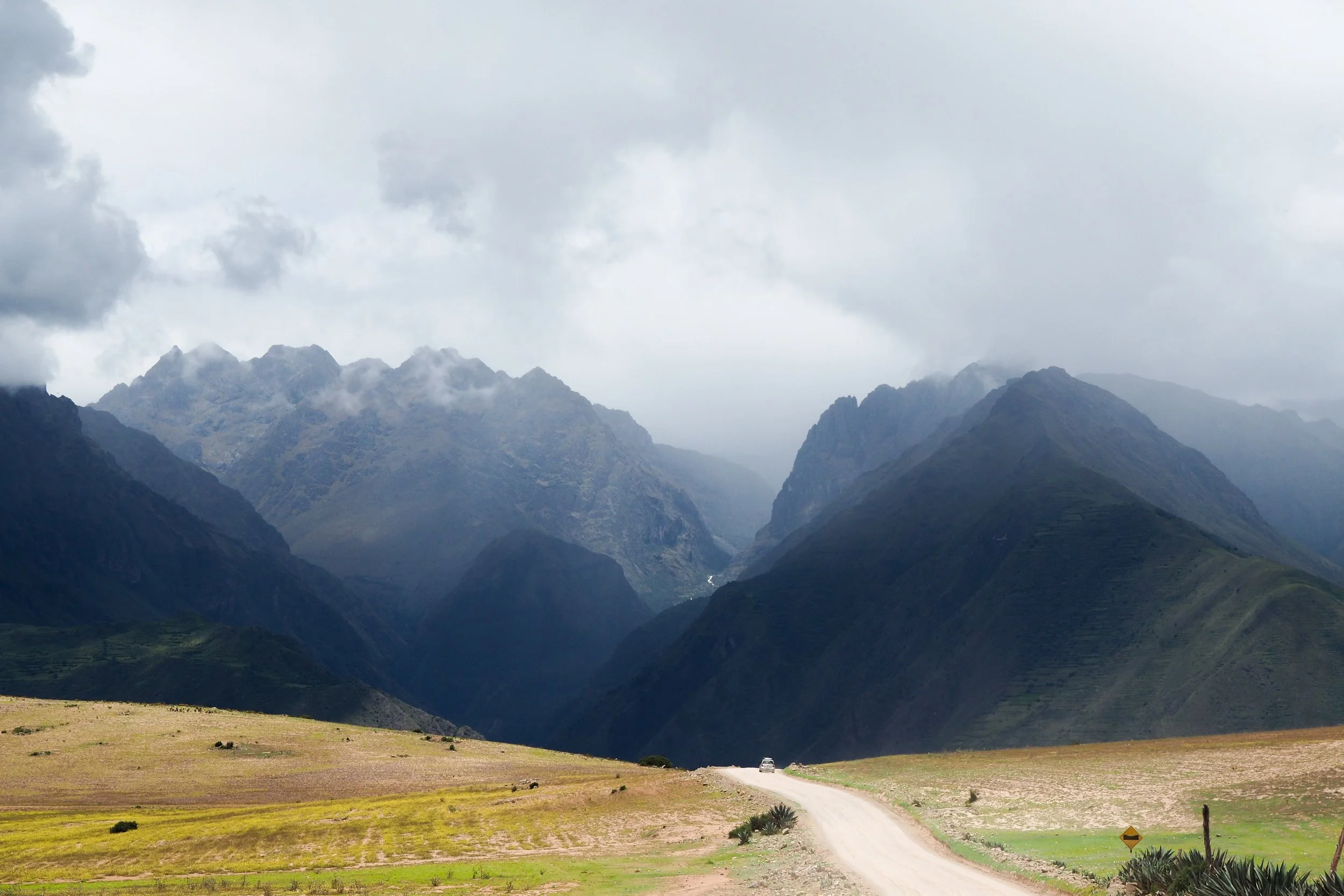 Peru: A dirt road running through a green valley with mountains covered in clouds in the background.