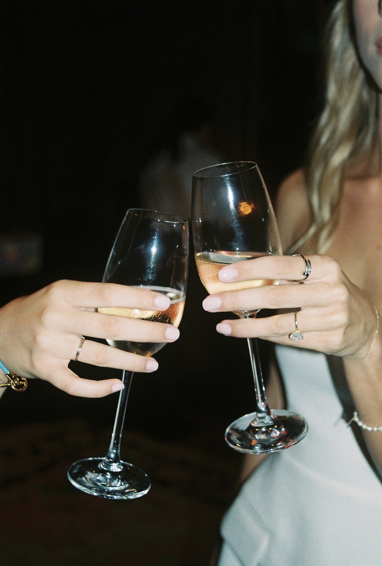 Two women holding glasses of champagne for a toast, with focus on their hands and rings.
